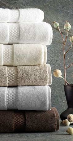 towels stacked on top of each other in front of a vase with flowers next to it