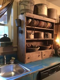 an old wooden shelf filled with dishes next to a sink in a room that has a window