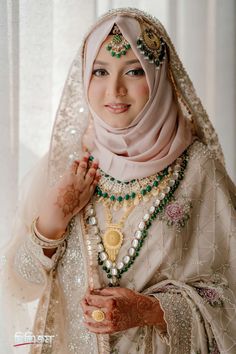 a woman wearing a hijab and jewelry poses for a photo in front of a window