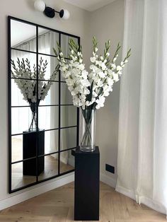 two vases filled with white flowers sitting on top of a wooden floor next to a mirror