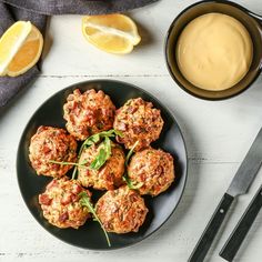 a black plate topped with meatballs next to a bowl of sauce and lemon wedges