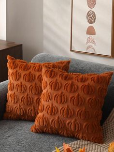 two orange pillows sitting on top of a blue couch in front of a framed painting