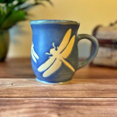 a blue and yellow coffee cup sitting on top of a wooden table next to a potted plant