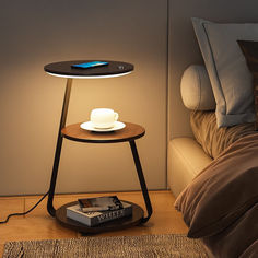 a small table with a cup on it next to a bed and a lamp that is turned on