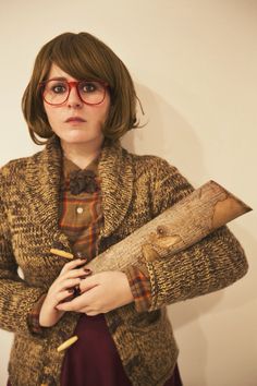 a woman wearing glasses and holding a piece of wood with her hands behind her back