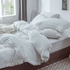 an unmade bed with white sheets and pillows on it in a bedroom next to a window