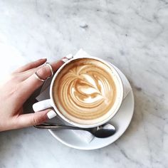 a person holding a cup of coffee on top of a white saucer