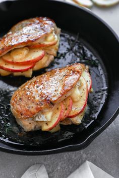 two pieces of meat with apple slices in a skillet on top of a table