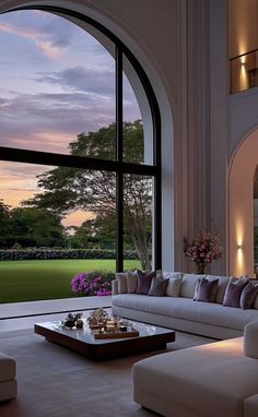 a living room filled with furniture and a large window overlooking a lush green field at sunset