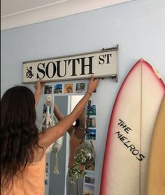 a woman holding up a sign that says south st in front of two surfboards