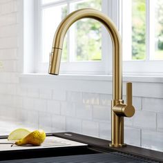 a kitchen sink with a gold faucet and some fruit on the counter top