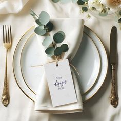 a place setting with white and gold plates, silverware and greenery on the table