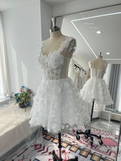 two white dresses are on display in front of a mirror, and one is being displayed