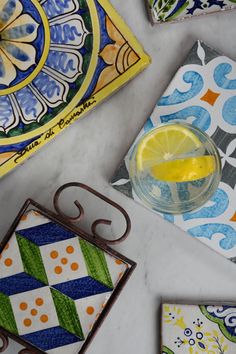 several colorful tiles and a glass with lemon on them sitting on a marble counter top