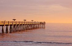 a long pier stretches out into the ocean at sunset with umbrellas in the foreground