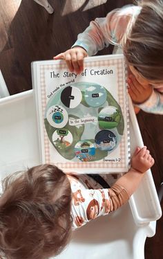 two young children looking at a book about the story of creation on a white tray