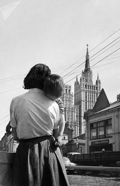 a black and white photo of a woman holding a child in her arms while looking at the city