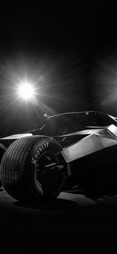 a black and white photo of a batmobile in the dark with its lights on