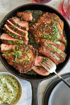 some meat is cooking in a skillet with sauce and garnishes on the side