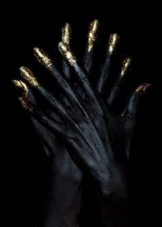 two hands with gold painted nails and black gloves