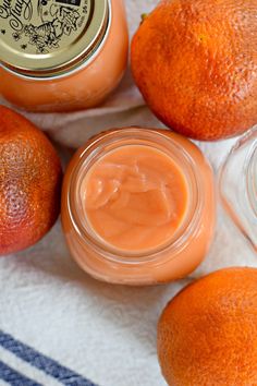 some oranges are sitting next to two jars and one is filled with something else