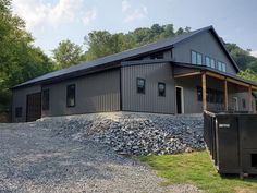 a large metal building sitting on top of a gravel covered field next to trees and grass