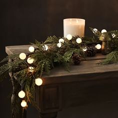 a table topped with a lit candle next to a pine cone and greenery wreath