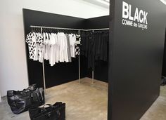 a black clothing store with clothes on racks and handbags in the foreground,