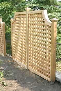 a wooden fence with lattice design in the middle and trees in the back ground behind it