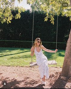 a woman in a white dress swinging on a tree swing