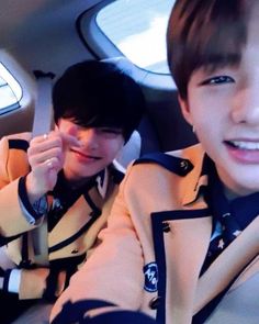 two young men sitting in the back seat of a car, one with his hand up to his face