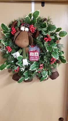 a christmas wreath hanging on the door with a teddy bear and holly wreath around it