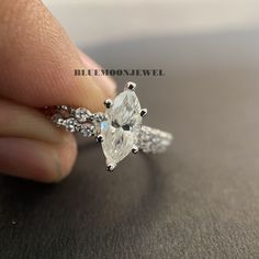 a person holding an engagement ring with two pear shaped diamonds on the band and side stones