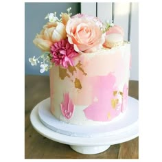 a pink and gold painted cake with flowers on the top is sitting on a white plate