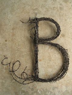 the letter b is made out of twigs and barbed wire on top of a cement floor