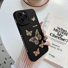 a woman is holding up her phone case with butterflies on it and an open book in the background