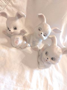 three white ceramic rabbits sitting on top of a bed next to each other and looking at the camera