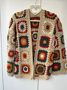 a crocheted jacket hanging on a wall with a hanger in front of it