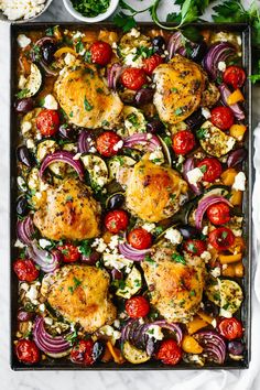 an overhead shot of chicken, tomatoes, onions and feta cheese on a baking sheet