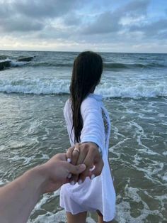 two people holding hands while standing in the water at the beach on a cloudy day