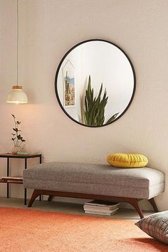 a living room with a round mirror on the wall and a bench in front of it