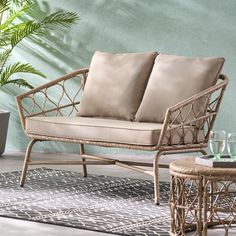 a wicker couch with two pillows on it next to a table and potted plant