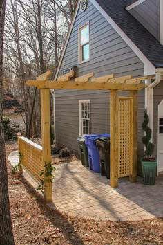 a house with a wooden pergolan on the front porch and trash cans in the yard