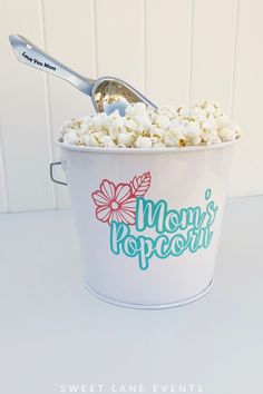 a white bucket filled with popcorn sitting on top of a table next to a spoon