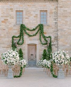 an outdoor ceremony set up with white flowers and greenery on the side of a stone building