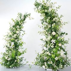 two white flowers and greenery are arranged in the shape of an arch