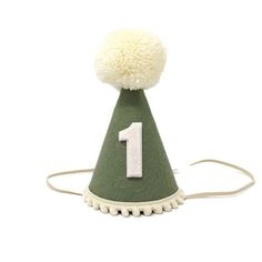 "Small 3\" or Large 5\" Olive Green Wool Felt hat, Cream yarn pom, Cream pom trim, with or without Linen Felt number backed in Linen. Our party hats and crowns are attached to a comfortable elastic and meant to be worn around the back of the head, behind the ears. Tilt to the side for a fun, whimsical look! LITTLE BLUE OLIVE SHOP CROWNS and HATS are the perfect accessory for birthday celebrations, memorable photo shoots and every day fun for dress up. Hats are hand crafted of a high quality, non Birthday Hat Felt, First Birthday Party Hat, First Birthday Neutral, Green First Birthday, Felt Party Hat, Green Birthday Party, First Birthday Hat, Neutral Party, Boys First Birthday