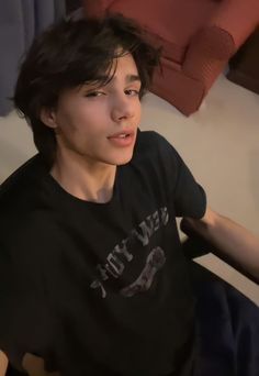 a young man sitting on top of a bed next to a red couch and pillows