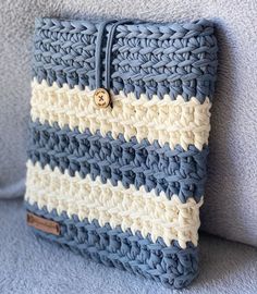 a blue and white crocheted pillow sitting on top of a gray couch with a button