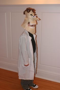 a person wearing a paper mask standing on a hard wood floor in front of a white wall